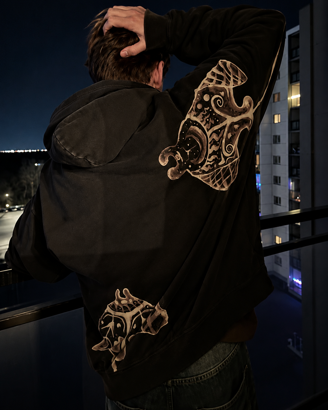 Black Manta bleach art hoodie with cream sleeve and back artwork on a balcony
